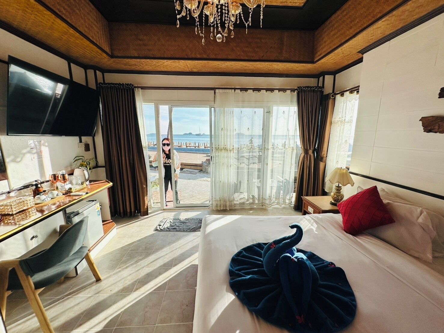 A hotel room with a bed, a desk, a TV, and a view of the beach.