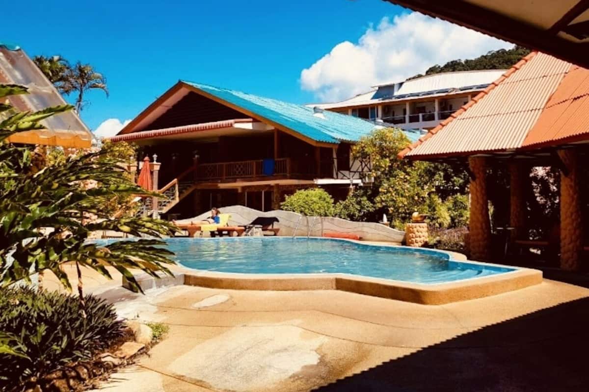 A resort with a swimming pool, multiple buildings with red roofs, and a clear blue sky.