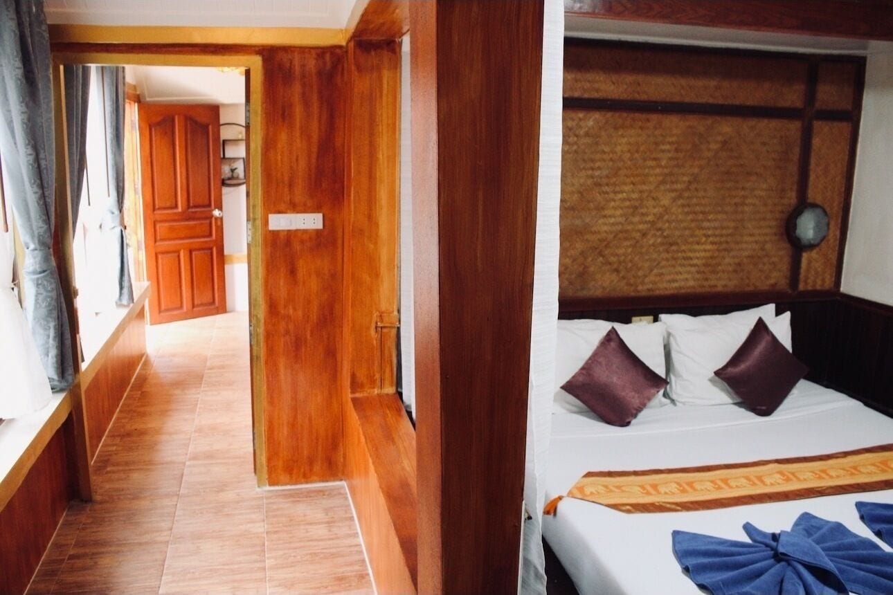 A hotel room with a wooden door, a bed with pillows, and a headboard with a textured panel.