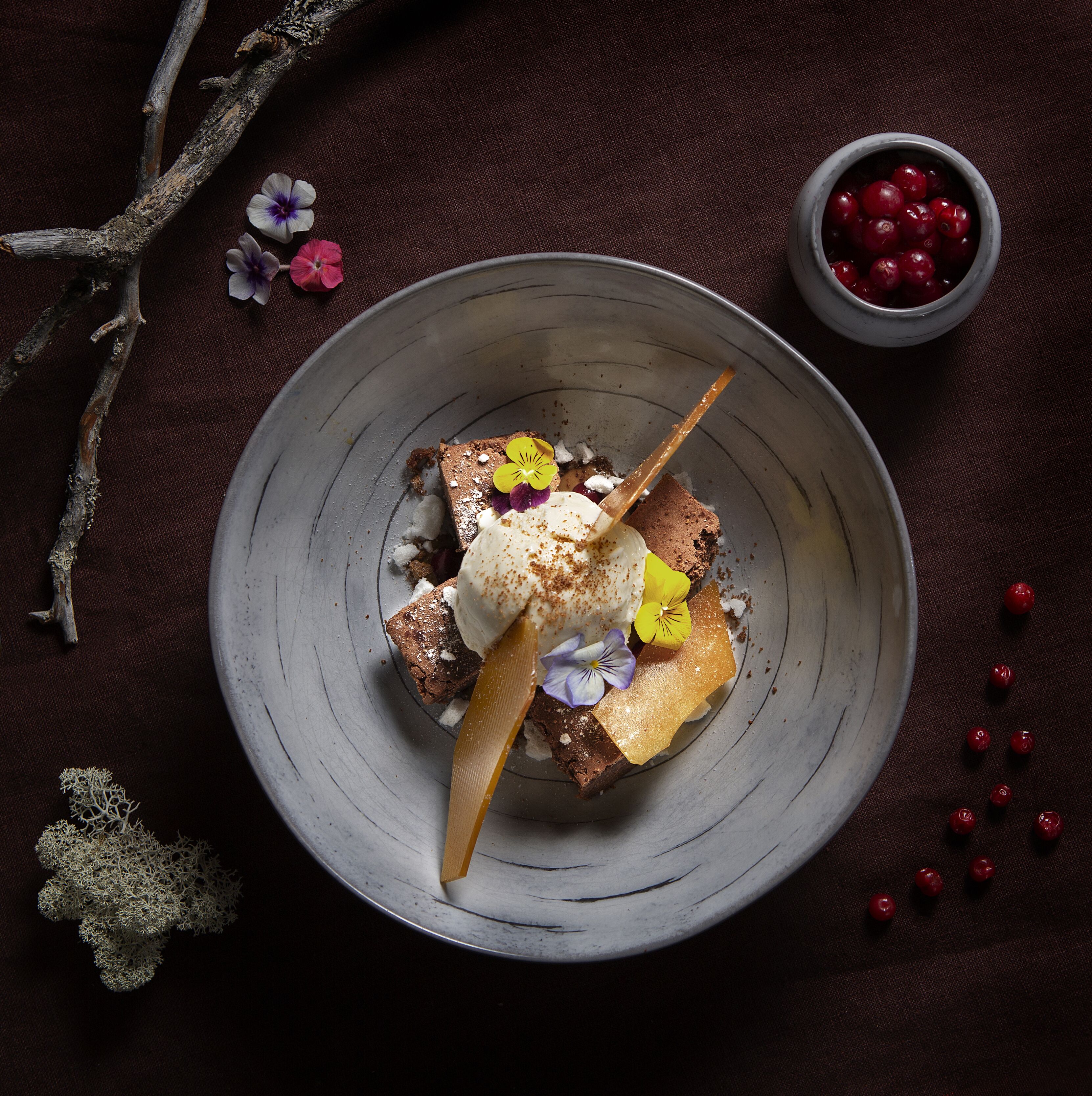 A dessert on a plate with a branch and flowers around it.