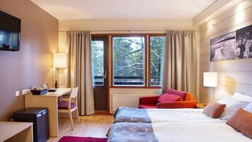 A hotel room with a bed, desk, chair, and a view of trees through the window.