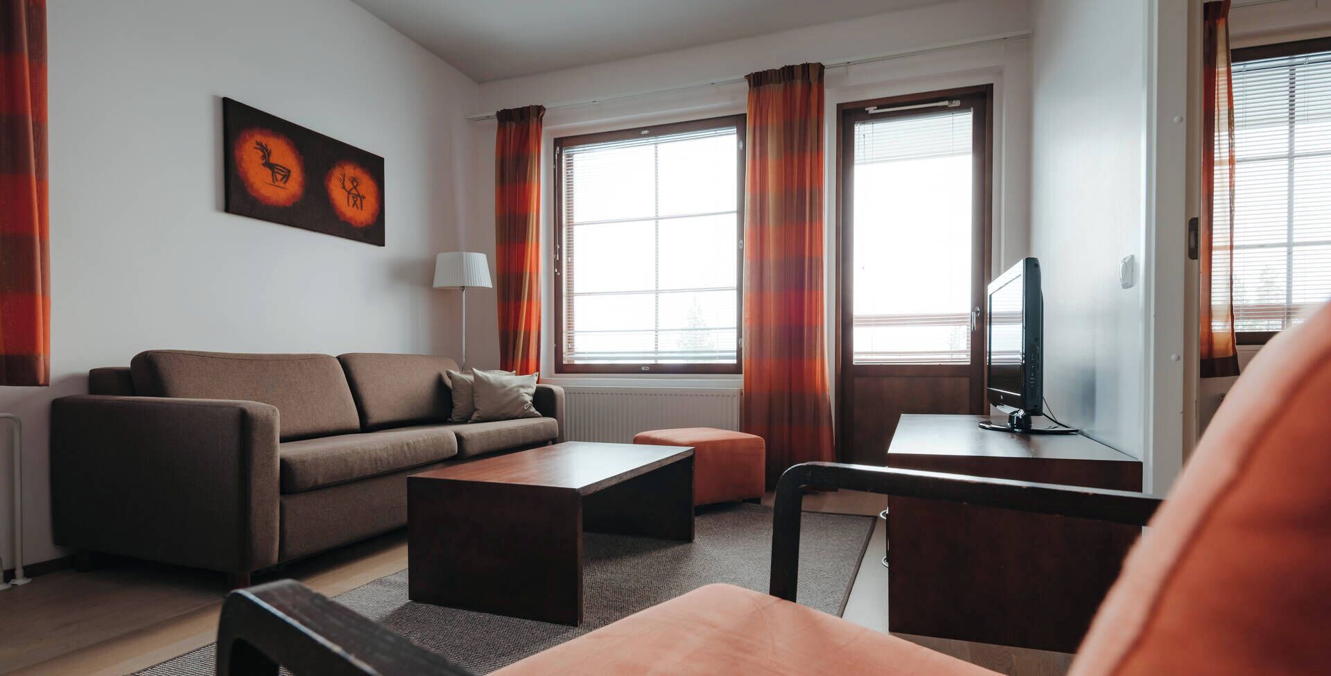 A modern living room with a sofa, coffee table, ottoman, TV, and artwork on the wall.