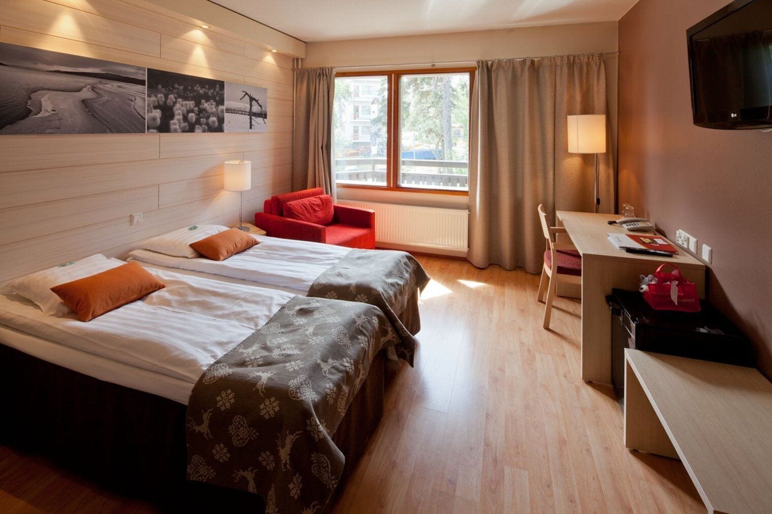 A hotel room with two beds, a desk, a chair, a TV, and a window with curtains.