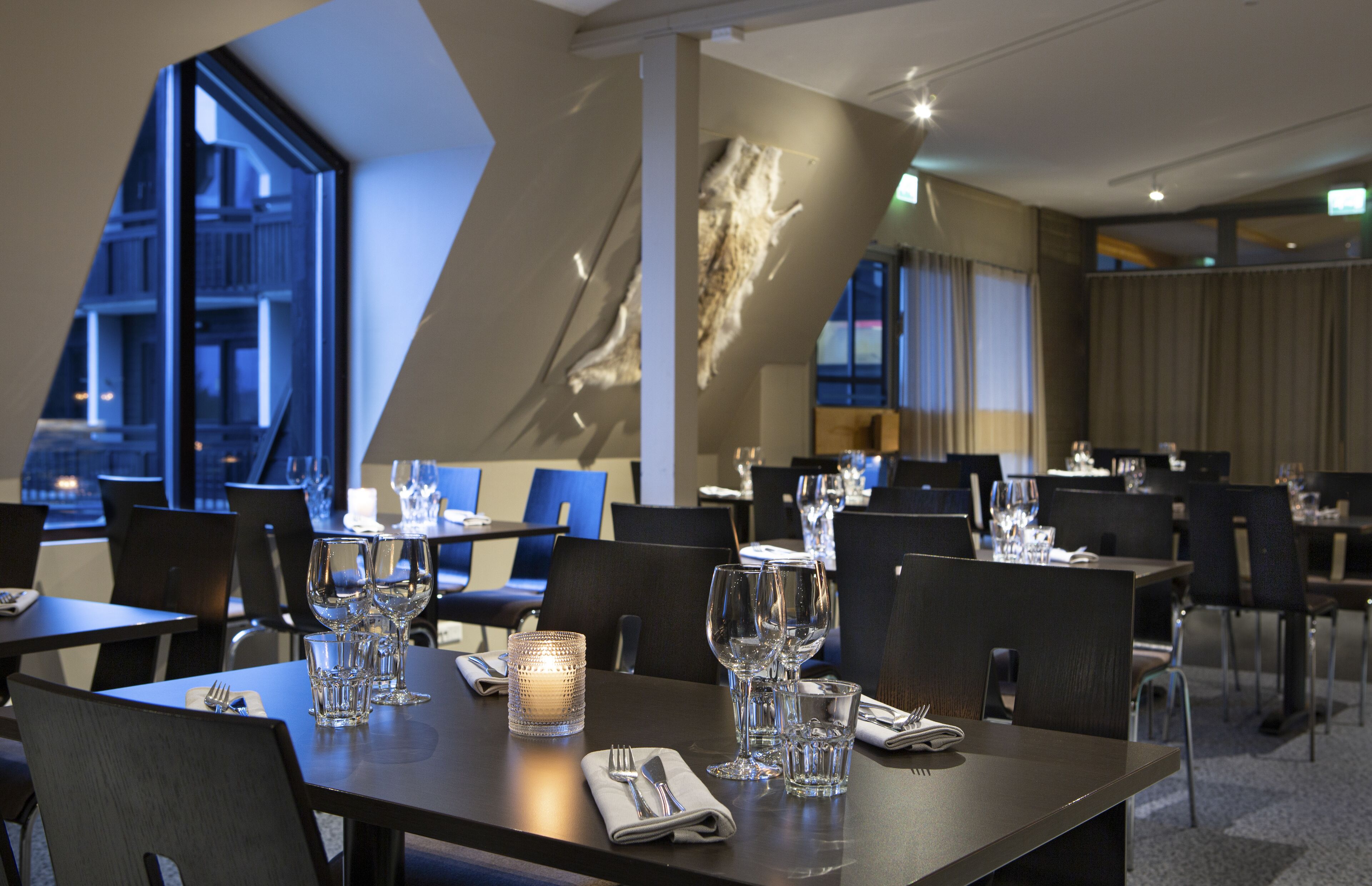 Un restaurante con mesas dispuestas para comer, con una decoración interior moderna y grandes ventanales que ofrecen vistas al exterior.