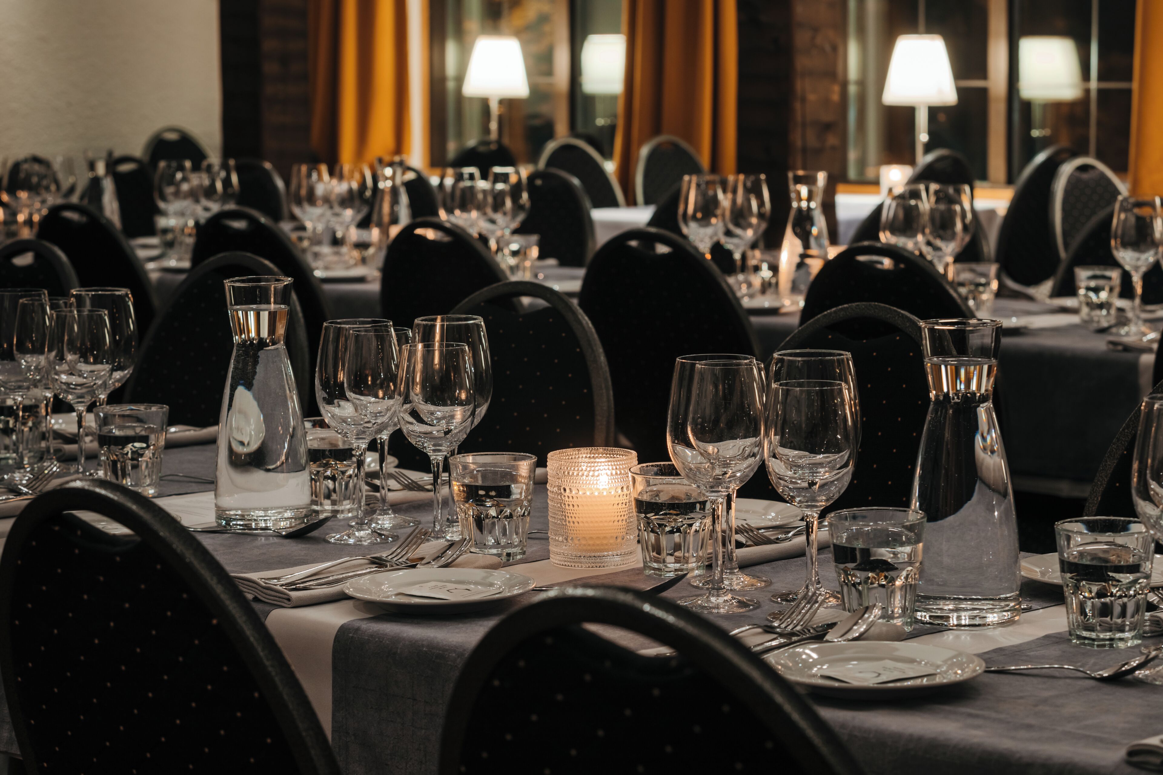 A dining table set with multiple chairs, glasses, and a candle centerpiece.