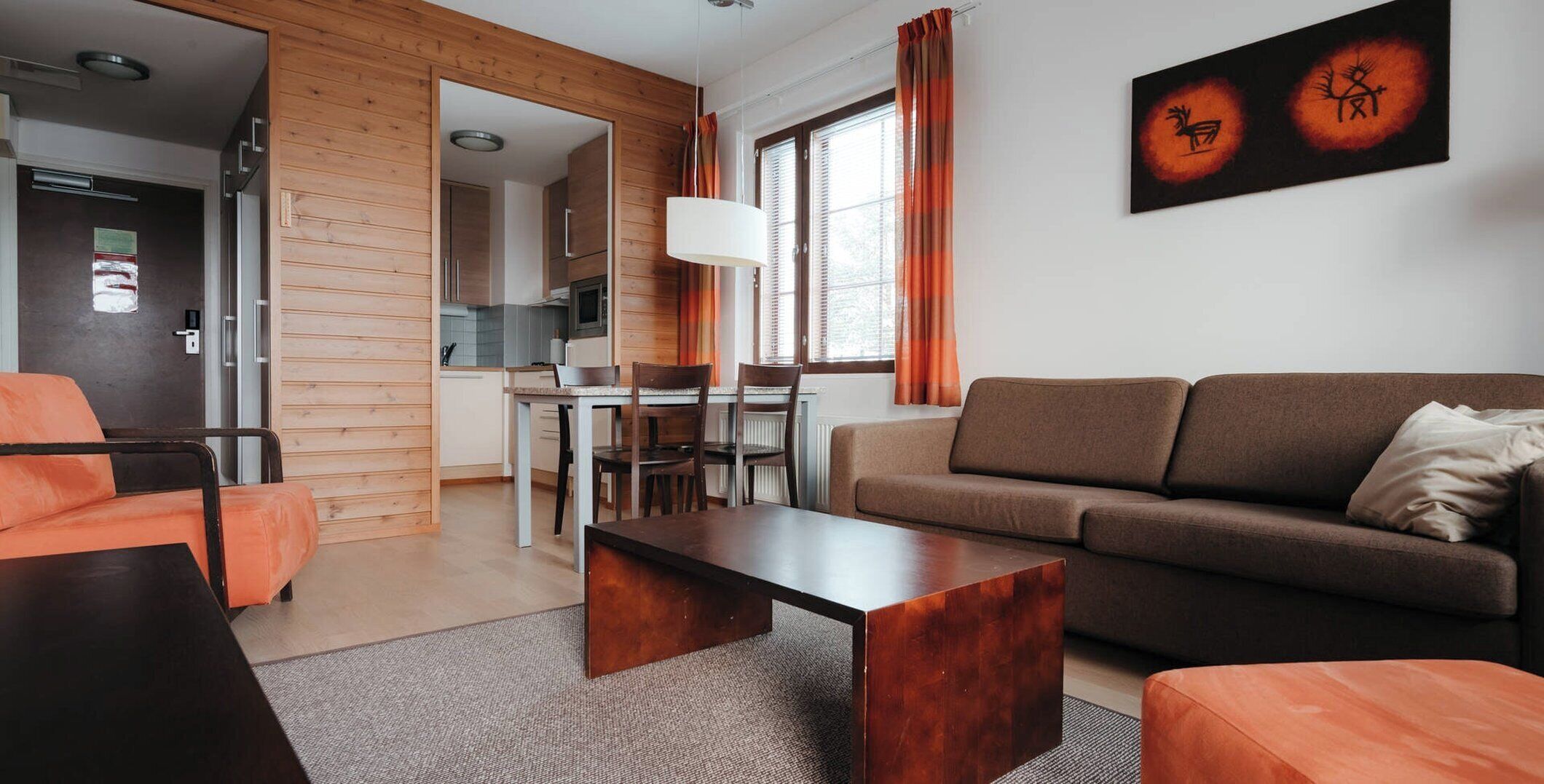 A modern living room with a sofa, coffee table, and chairs, a dining area with a table and chairs, and a kitchen in the background.