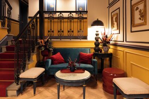 A room with a staircase, a blue sofa with red cushions, a round table with a tray, and a red ottoman. - JOIVY Together Florence Secret Nest (Florence)