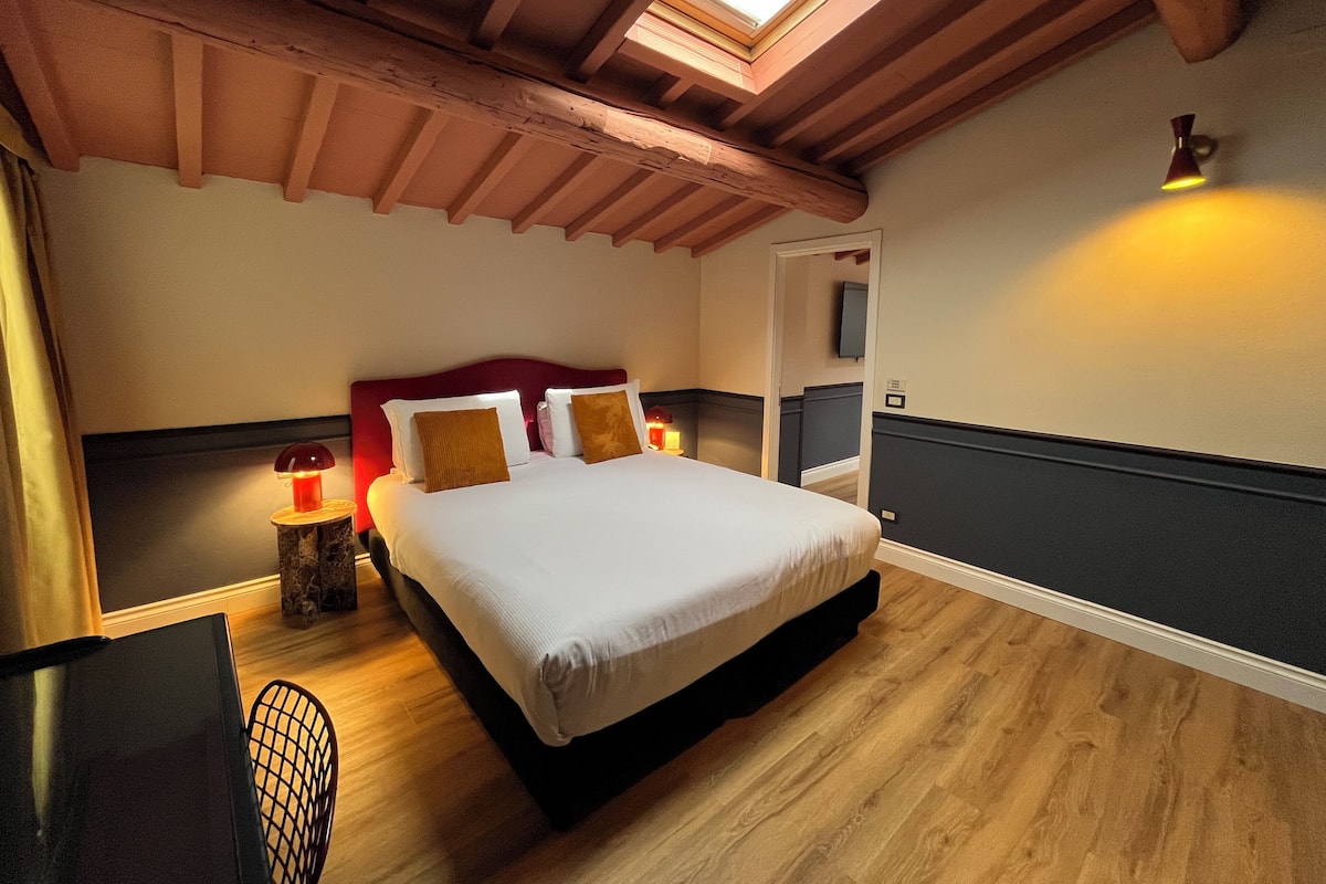 A bedroom with a wooden ceiling, a bed with white bedding, a nightstand with a lamp, and a chair.