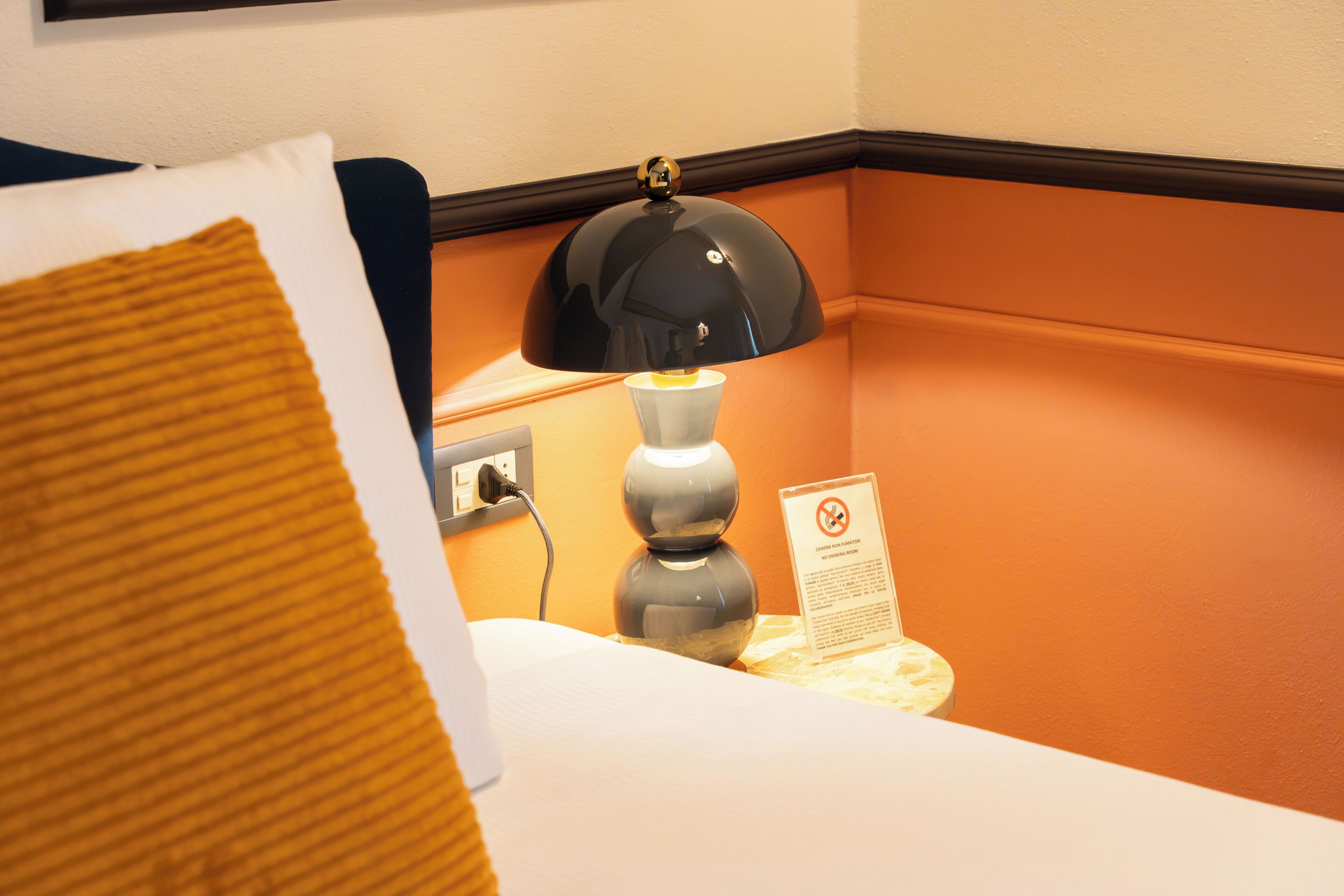 Ein Hotelzimmer mit einem Bett, einem Nachttisch, einer Lampe und einem Schild mit einem Rauchverbotssymbol.