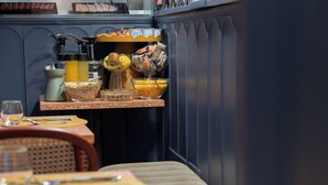 A breakfast bar with a variety of food items and condiments, a coffee machine, and a seating area with a table set for two. - JOIVY Together Florence Secret Nest (Florence)