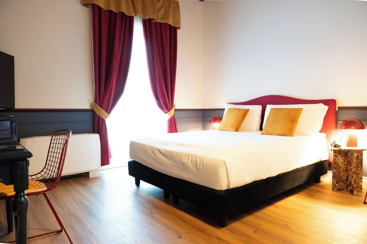 A hotel room with a bed, a chair, a table, and a radiator.