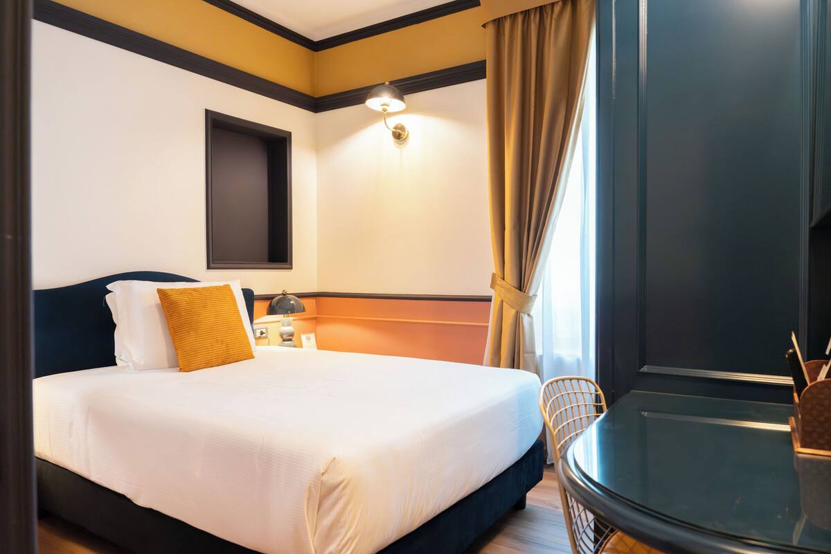 A hotel room with a bed, a nightstand, a lamp, a chair, and a glass table.