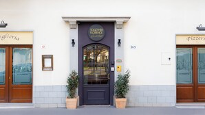 A building facade with a dark entrance door, two potted plants, and signage for 'TOGETHER Florence' and 'Pizzeria.' - JOIVY Together Florence Secret Nest (Florence)