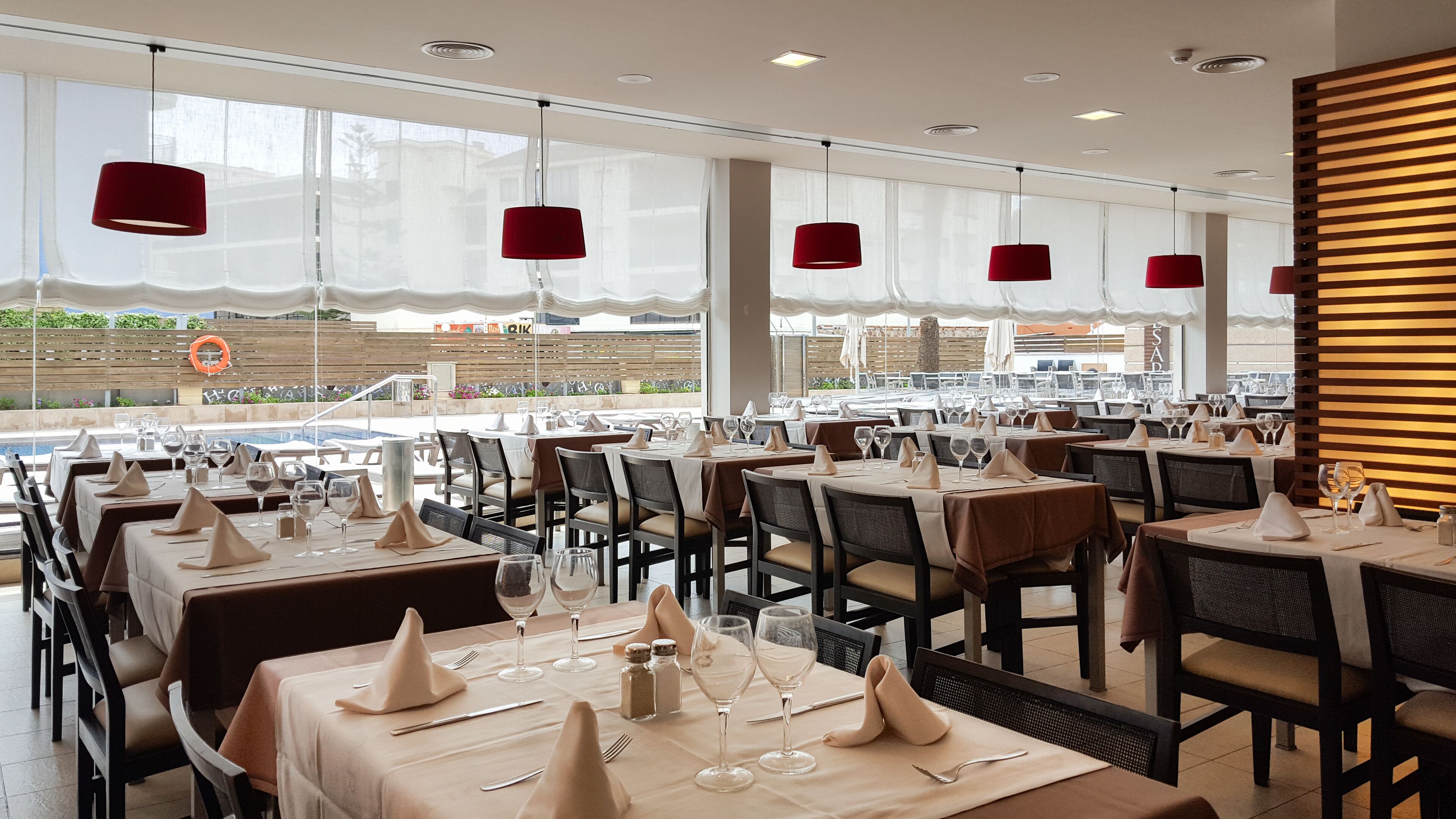 Ein Restaurant mit mehreren Tischen, bereit zum Essen, mit Blick auf einen Pool und Gebäude im Hintergrund.