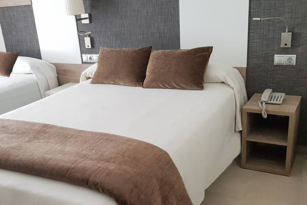 A hotel room with a large bed, two pillows, a bedside table with a phone, and a wall socket.
