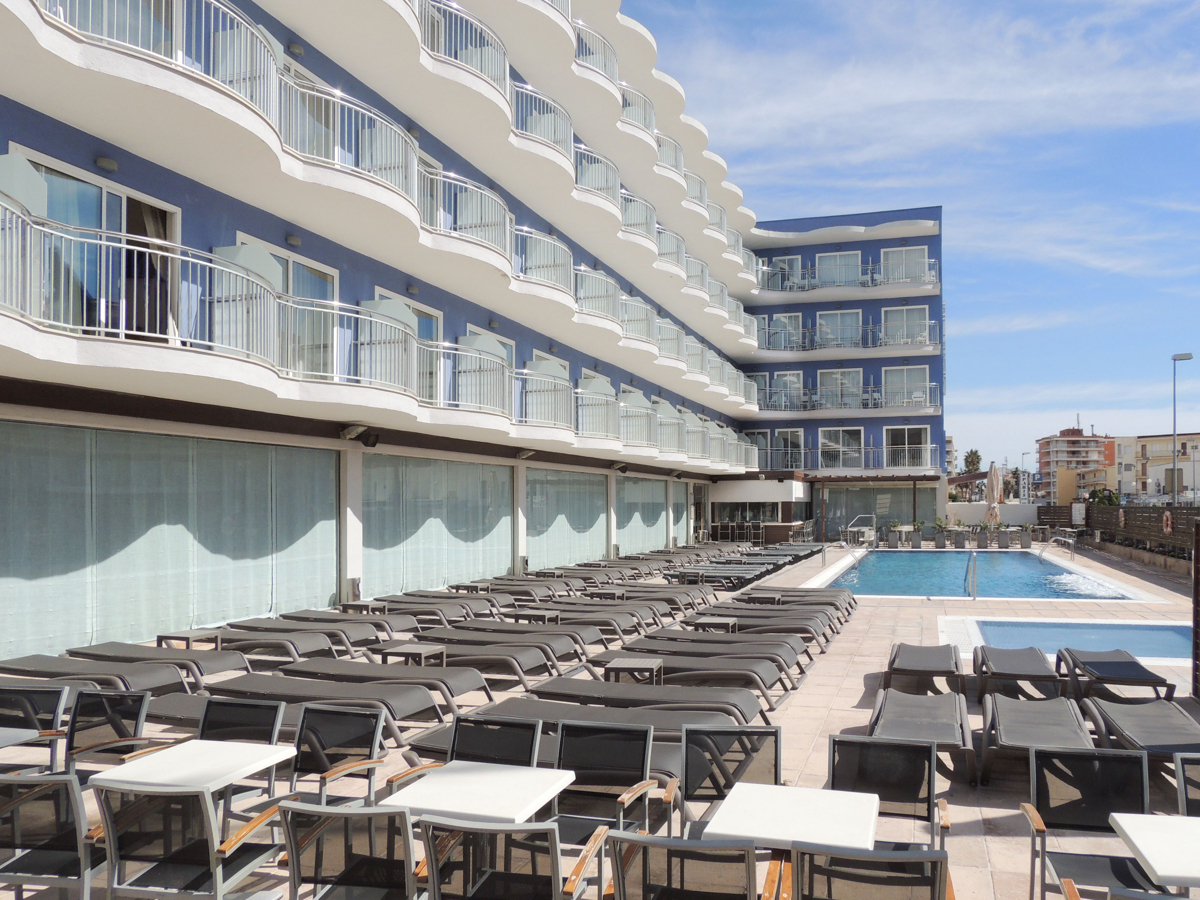 A hotel with multiple balconies, a swimming pool, and sun loungers.