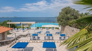 Zona junto a la piscina con mesas y sillas azules, un área de estar cubierta y vista al mar.
