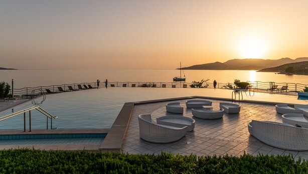 Zona de piscina con mobiliario y vista al atardecer sobre el agua.