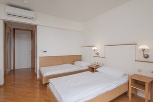 Habitación de hotel con dos camas individuales, cabeceros de madera, mesitas de noche y un ventilador de aire acondicionado.