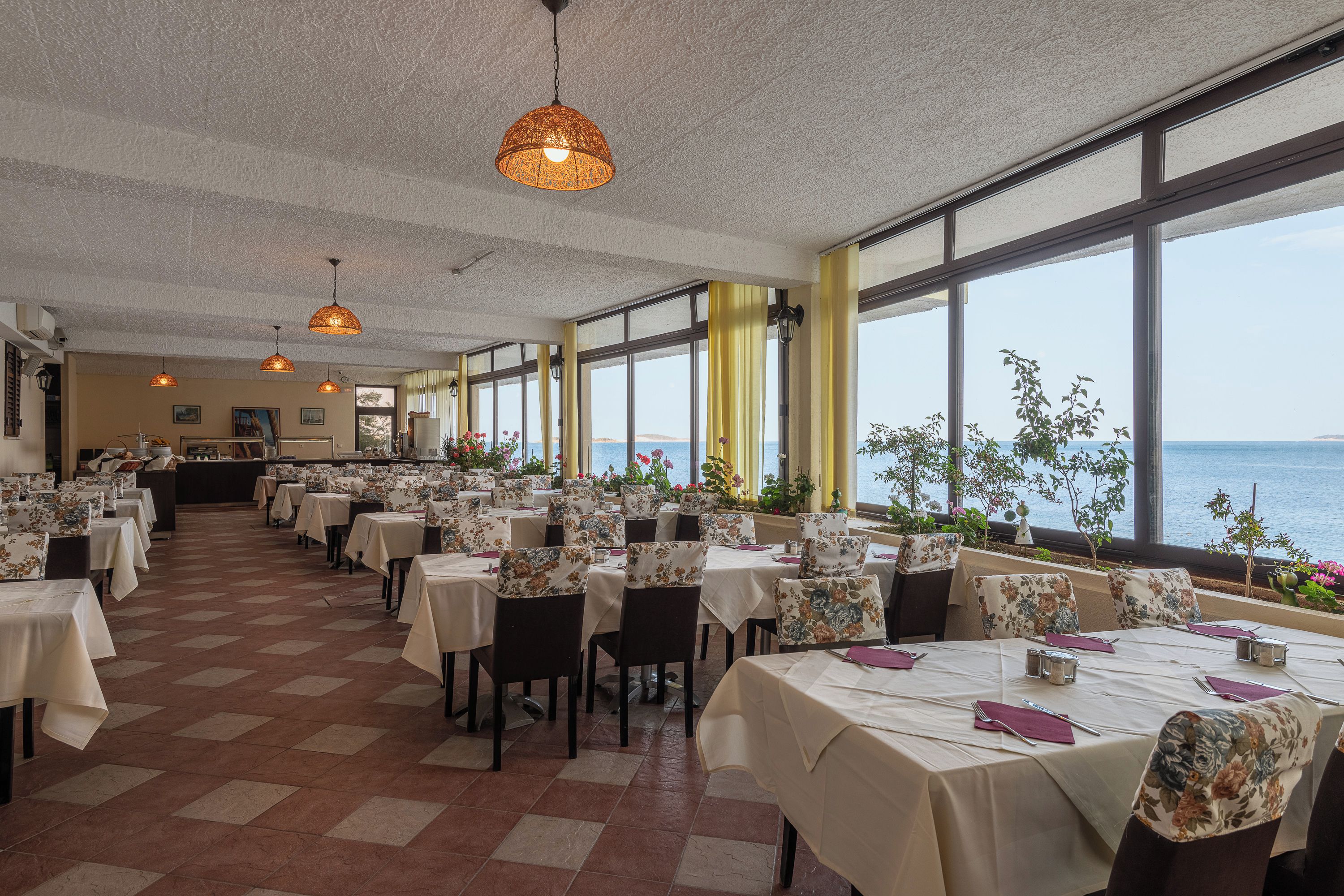 Restaurante com várias mesas, cadeiras e luminárias pendentes.