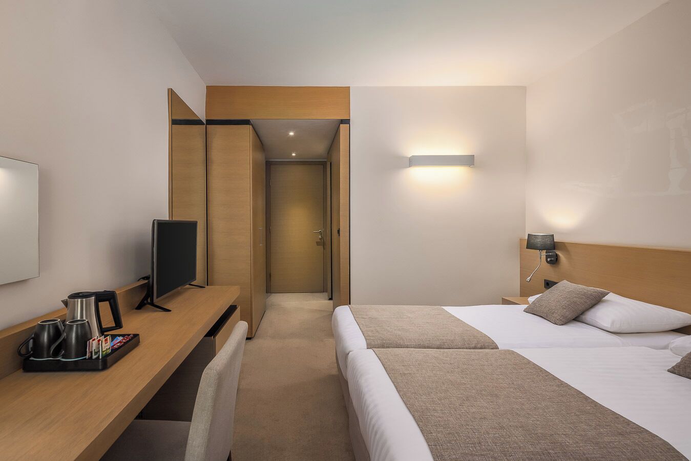 A hotel room with a bed, bedside table, TV, and a desk with a coffee maker.