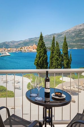 A balcony with a table, a bottle of wine, and a bowl of nuts, overlooking a body of water and a coastal town. - Aminess Liburna Hotel  (Korcula)