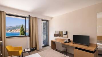 Habitación de hotel con cama, escritorio, silla, televisor y ventana con vista a un pueblo costero.