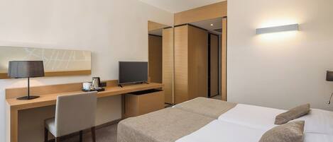 A hotel room with a bed, a desk with a computer, a chair, and a small table with a bowl of snacks.