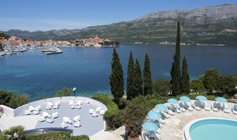A coastal resort with a pool area, lounge chairs, and a view of the marina and mountains.