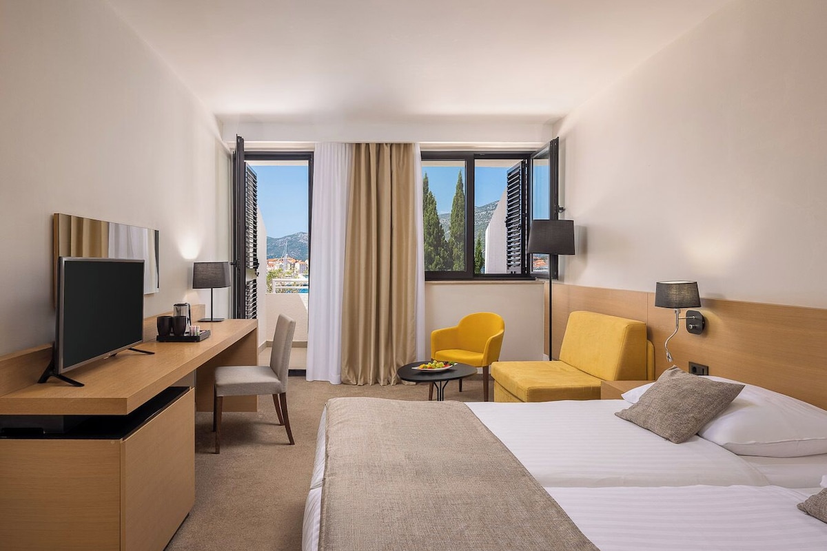 A hotel room with a bed, a desk with a computer, a chair, a small table, and a sofa.