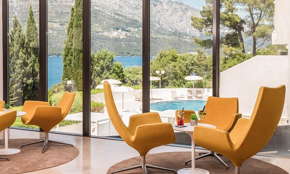 A modern outdoor seating area with yellow chairs and a table, overlooking a pool and a mountainous landscape. - Aminess Liburna Hotel  (Korcula)