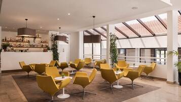 A modern lounge area with yellow chairs, a bar with various bottles, and large windows allowing natural light.