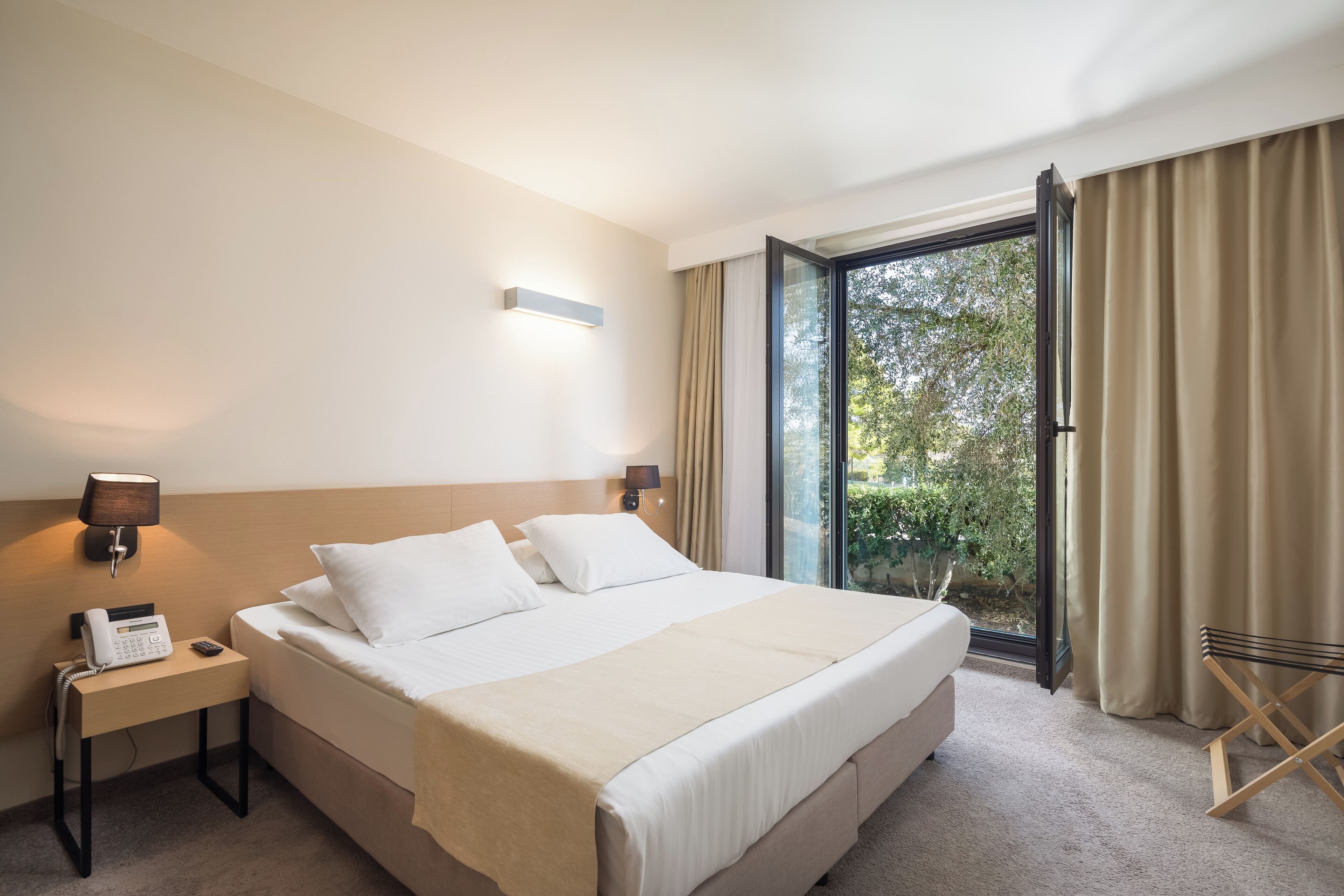 A hotel room with a bed, bedside lamps, a telephone, and a window with curtains.
