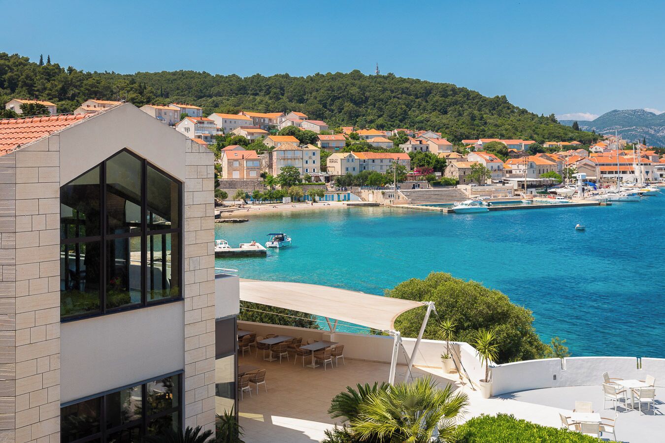 Une ville côtière qui abrite un bâtiment moderne doté de grandes fenêtres et d’un patio aménagé avec du mobilier d’extérieur.