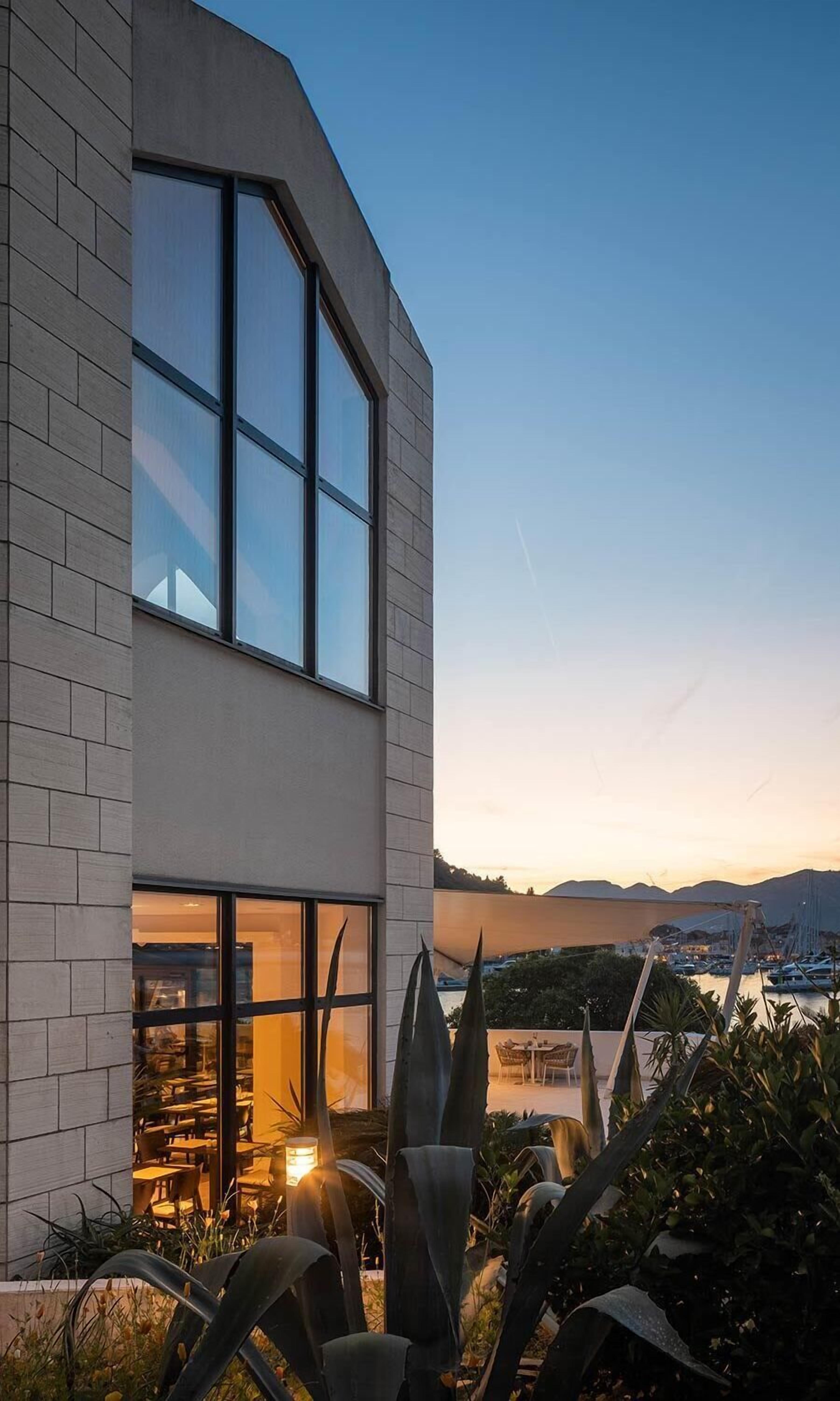 A modern building with large windows and a view of a marina at sunset.
