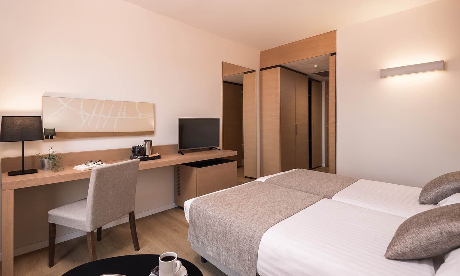 A hotel room with a bed, a desk with a computer, a chair, a TV, and a mirror.