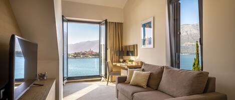 A hotel room with a large window, a sofa, a TV, and a desk with a chair.