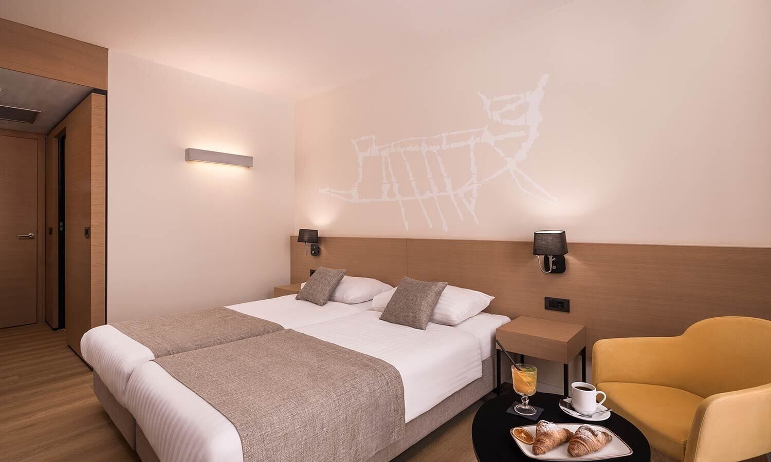 Een hotelkamer met een bed, twee nachtkastjes, een stoel en een wandprojectie.