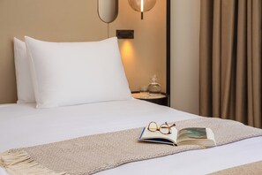 Ein ordentlich bezogenes Bett mit weißen Leinen, eine Brille und ein offenes Buch auf einer beigen, strukturierten Decke.