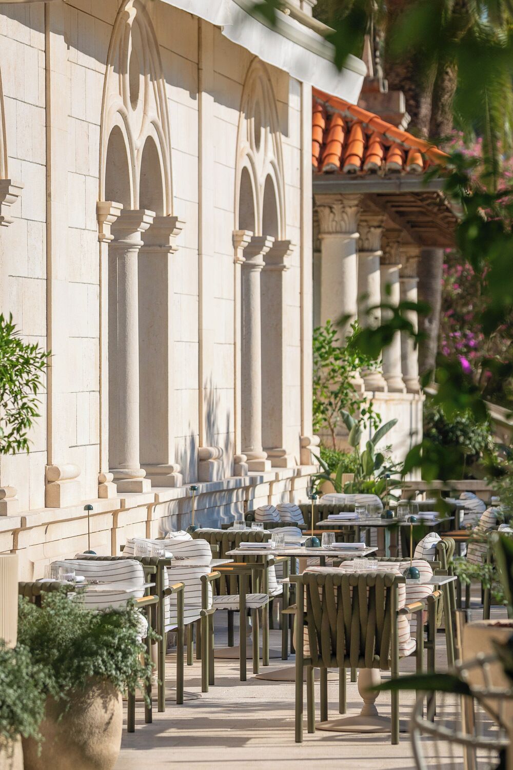 An outdoor seating area with tables and chairs, a building with classical architecture, and a tiled roof.