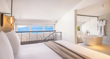 Un dormitorio moderno con una cama grande, vistas al mar y un baño separado con bañera independiente.