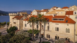 Un edificio histórico con un patio, palmeras y vistas al mar.