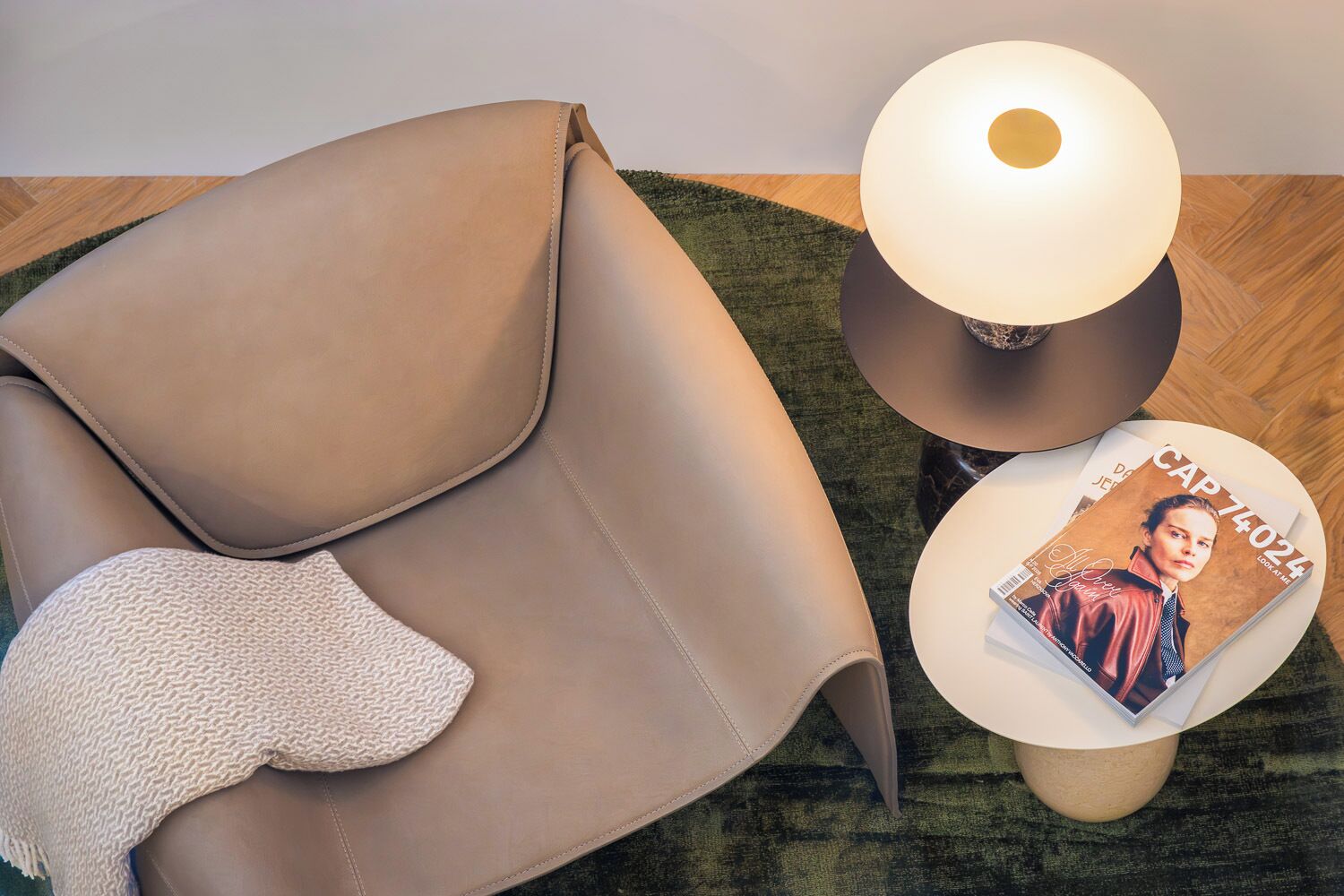 A modern living room with a leather sofa, a round side table with a magazine, and a floor lamp.
