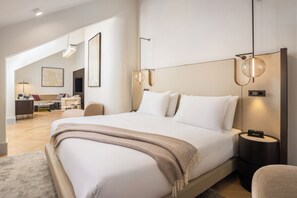 Een moderne hotelkamer met een groot bed, een zithoek met een bank en fauteuils, en een eettafel.