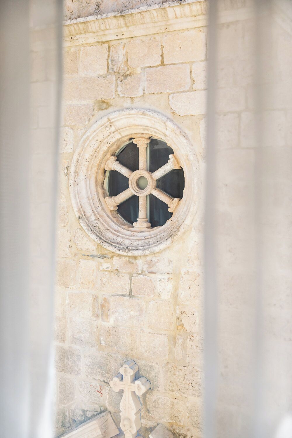 A stone wall with a circular window featuring a cross at its base.