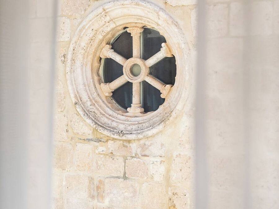 A stone wall with a circular window featuring a cross at its base.