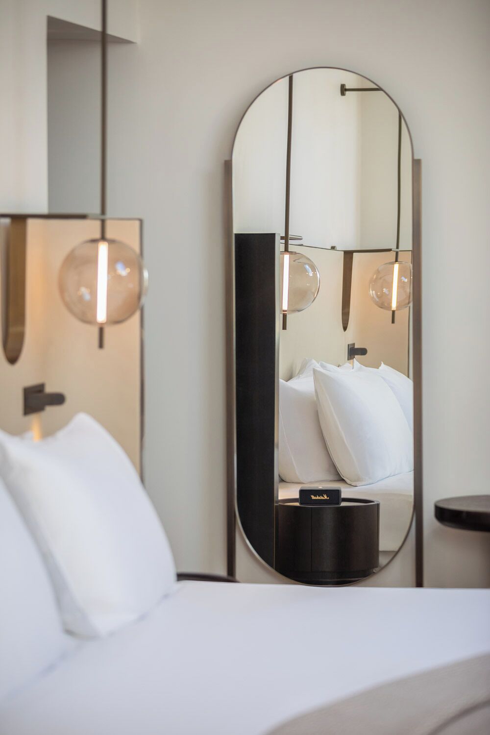 A hotel room with a bed, a large mirror, a bedside table, and a lamp.