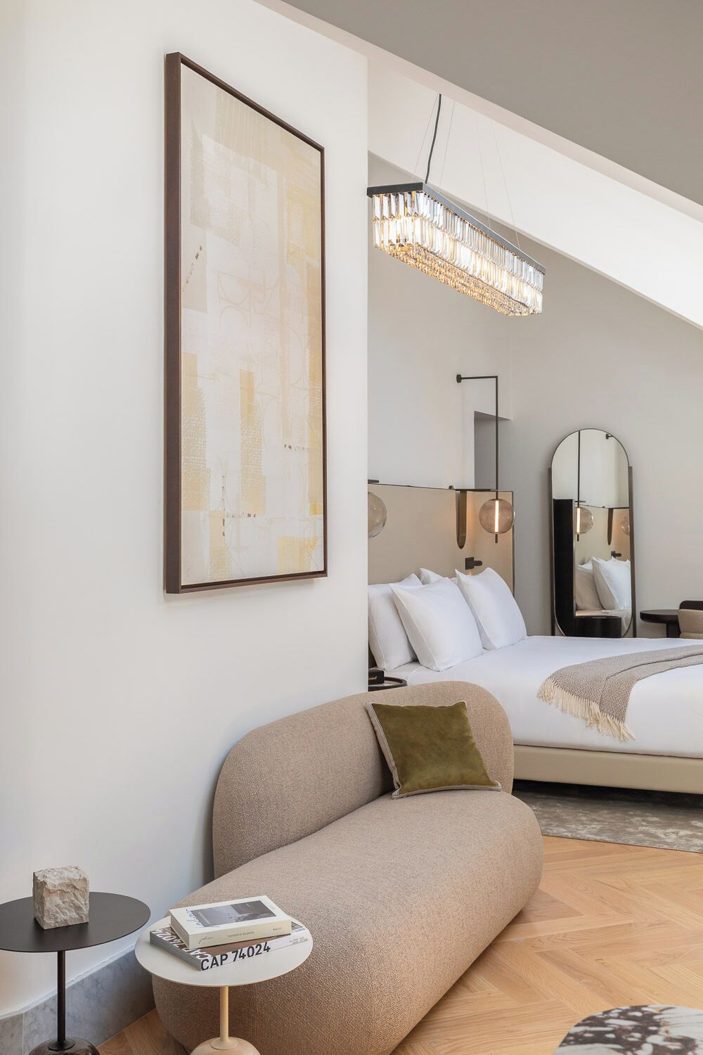 Habitación de hotel moderna con cama, sofá, una mesita con un libro, una obra de arte enmarco y una araña.