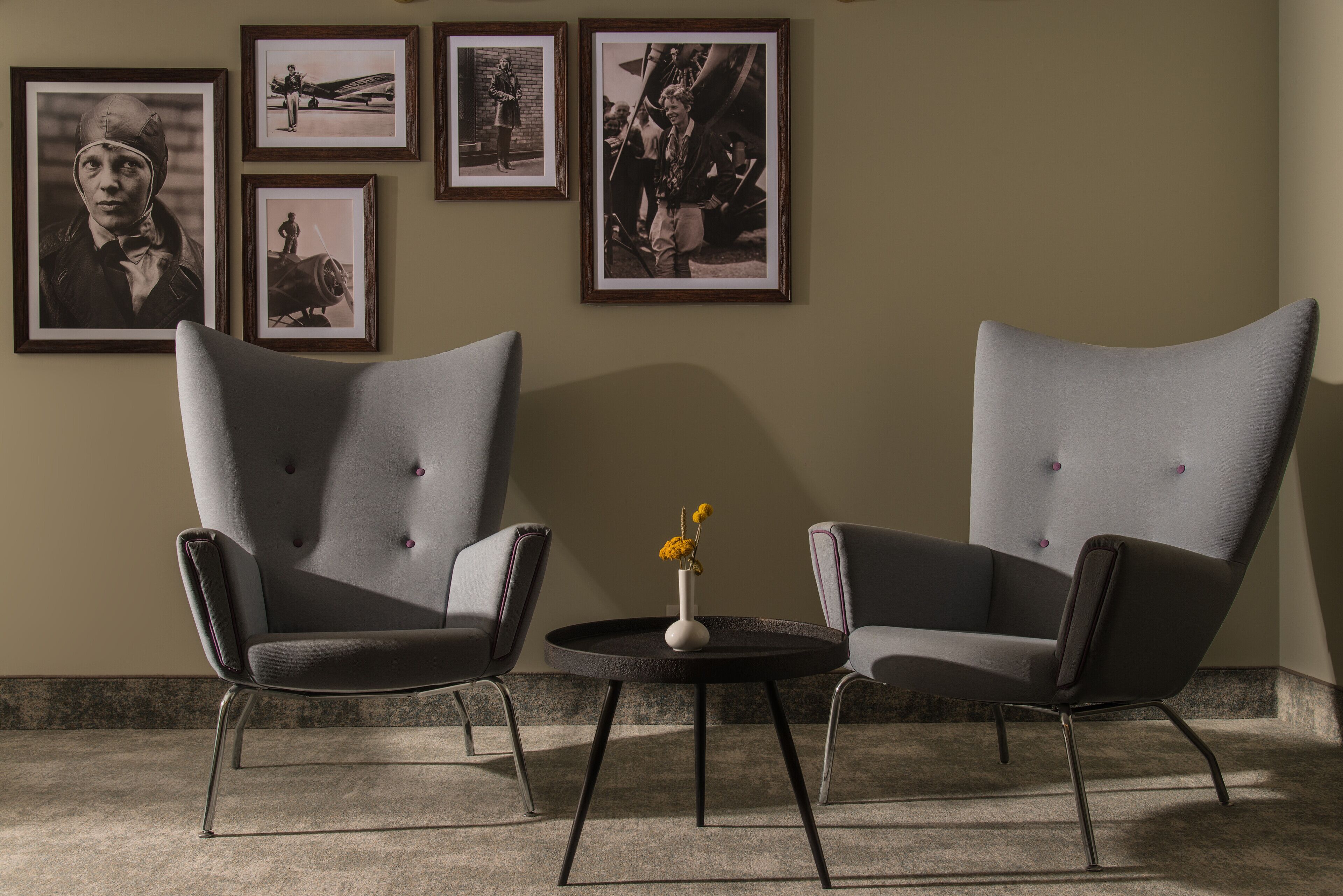 Two modern armchairs facing each other with a small round table between them, featuring a vase with flowers.