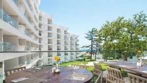 A dining area with a wooden table and chairs, overlooking a pool and a garden.